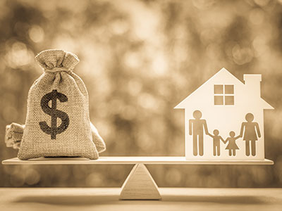 Sepia-toned scale: Money bag with dollar sign on left, balanced by cut-out house and family on right. Equilibrium of wealth and family life.