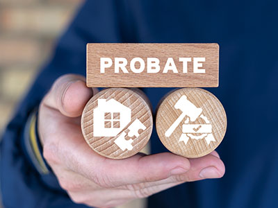 A hand holds wooden tokens: “PROBATE” sign, house icon, and gavel icon. Legal theme.
